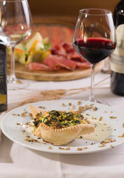 Tavola apparecchiata con vino rosso, olio d'oliva e piatto gourmet.