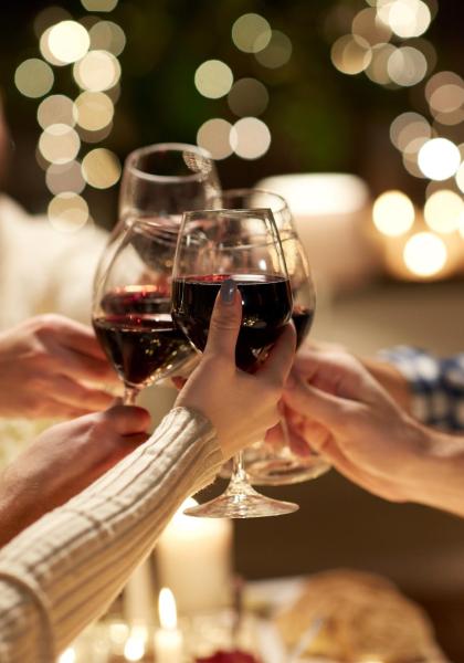 Friends toasting with red wine glasses, soft lights in the background.