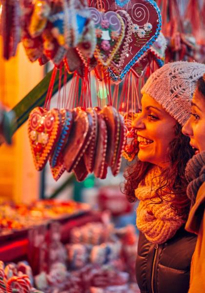 Two smiling women look at heart-shaped sweets at a market.