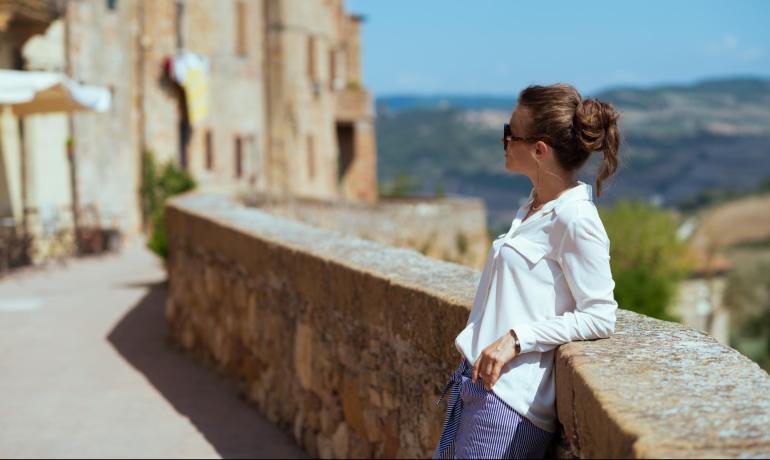 Donna con occhiali da sole guarda il paesaggio da un muro di pietra.