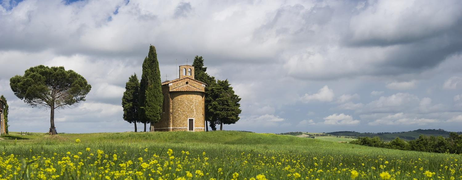 Lonely chapel in Tuscan countryside, surrounded by cypress trees.